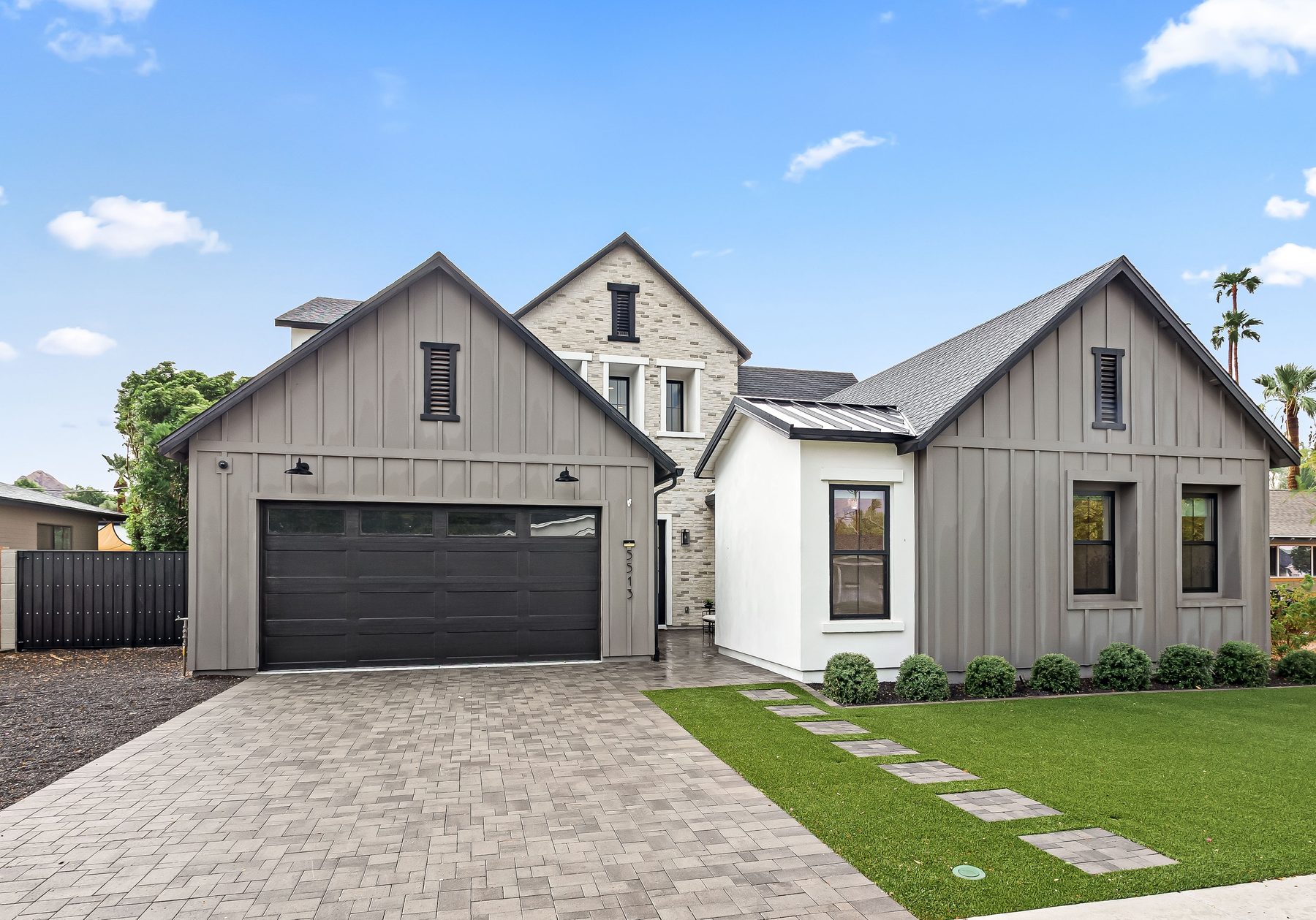 Front elevation of 5513 E Verde Lane with board and batten, stone, paver driveway, and lawn in Lower Arcadia